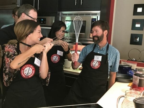 A group of people in a kitchen with a whisk participating in team-building cooking classes.