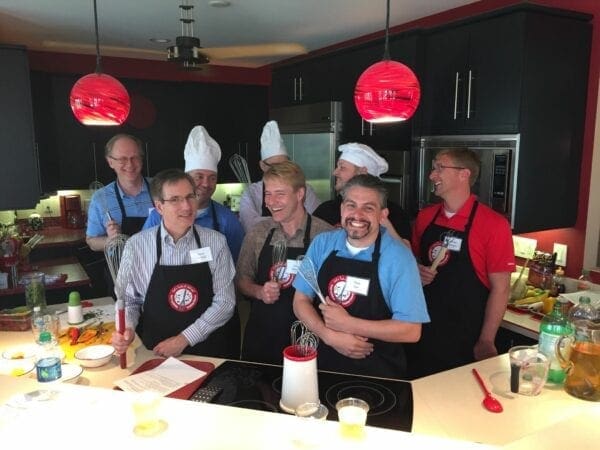 A group of people posing for a picture in a kitchen during team-building cooking classes.