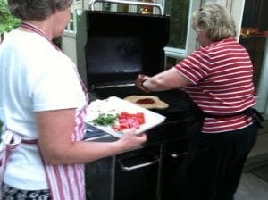A woman is preparing a pizza on a grill at a cooking class in Eastern Iowa.
