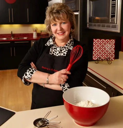 A woman in an apron is participating in a team-building cooking class, standing in front of a bowl of flour.