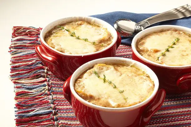 Three red mugs filled with soup on a table.