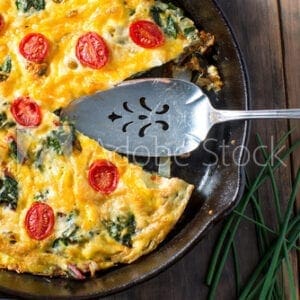 Quiche with spinach and tomatoes in a skillet.