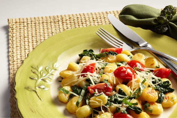 Gnocchi with spinach and tomatoes on a green plate.