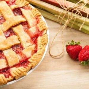 A pie with strawberries and rhubarb on a wooden table.