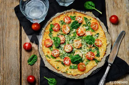 A pizza with spinach and tomatoes on a wooden table.