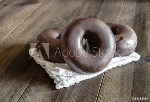 Three chocolate donuts on a wooden table.